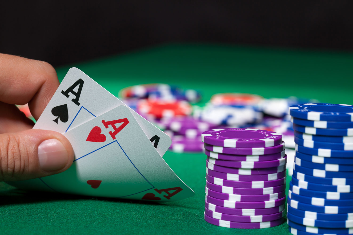 Poker - An individual hold a pair of aces, sitting behind a stack of poker chips