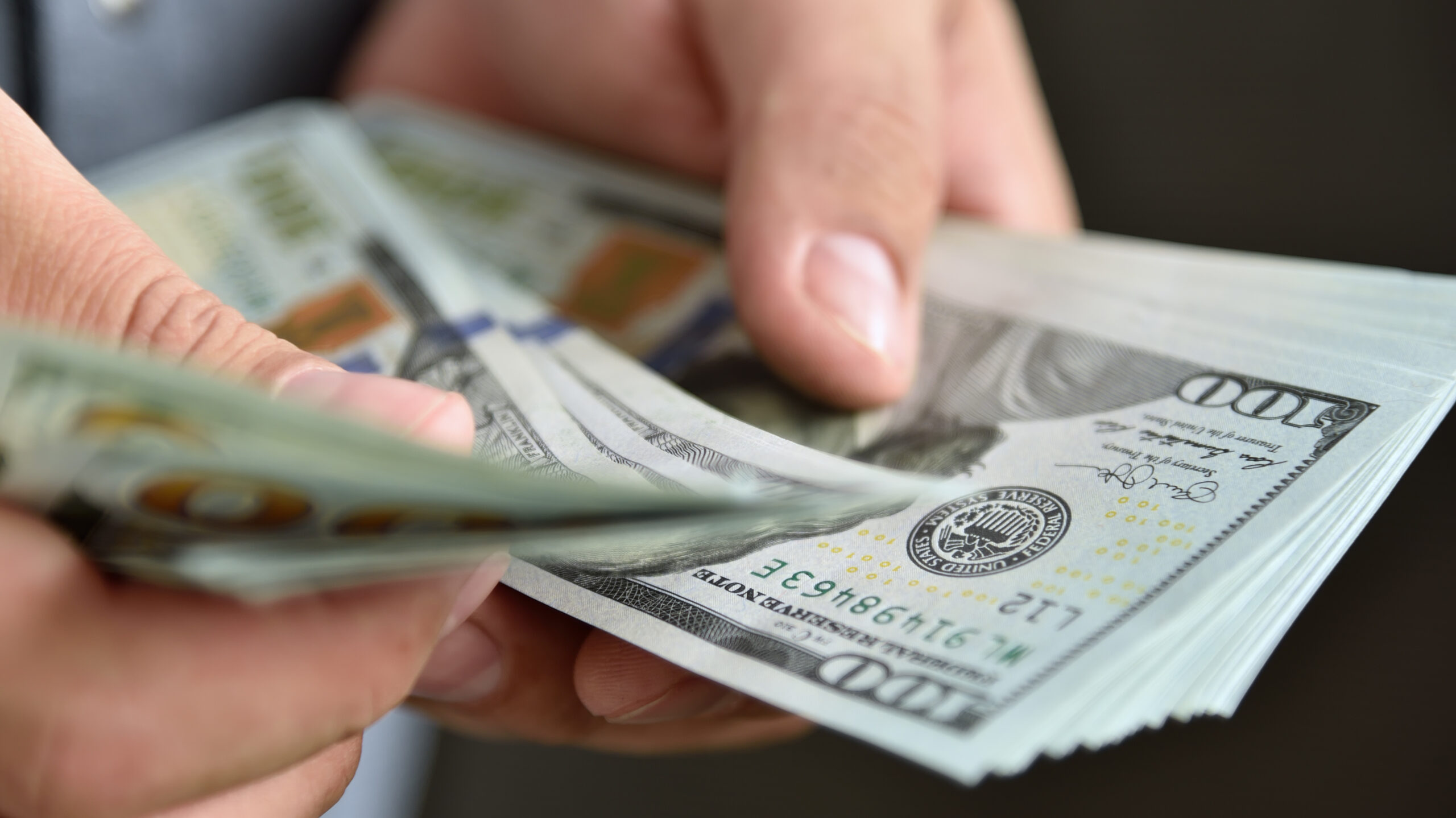 A person counting a stack of 100 dollar bills